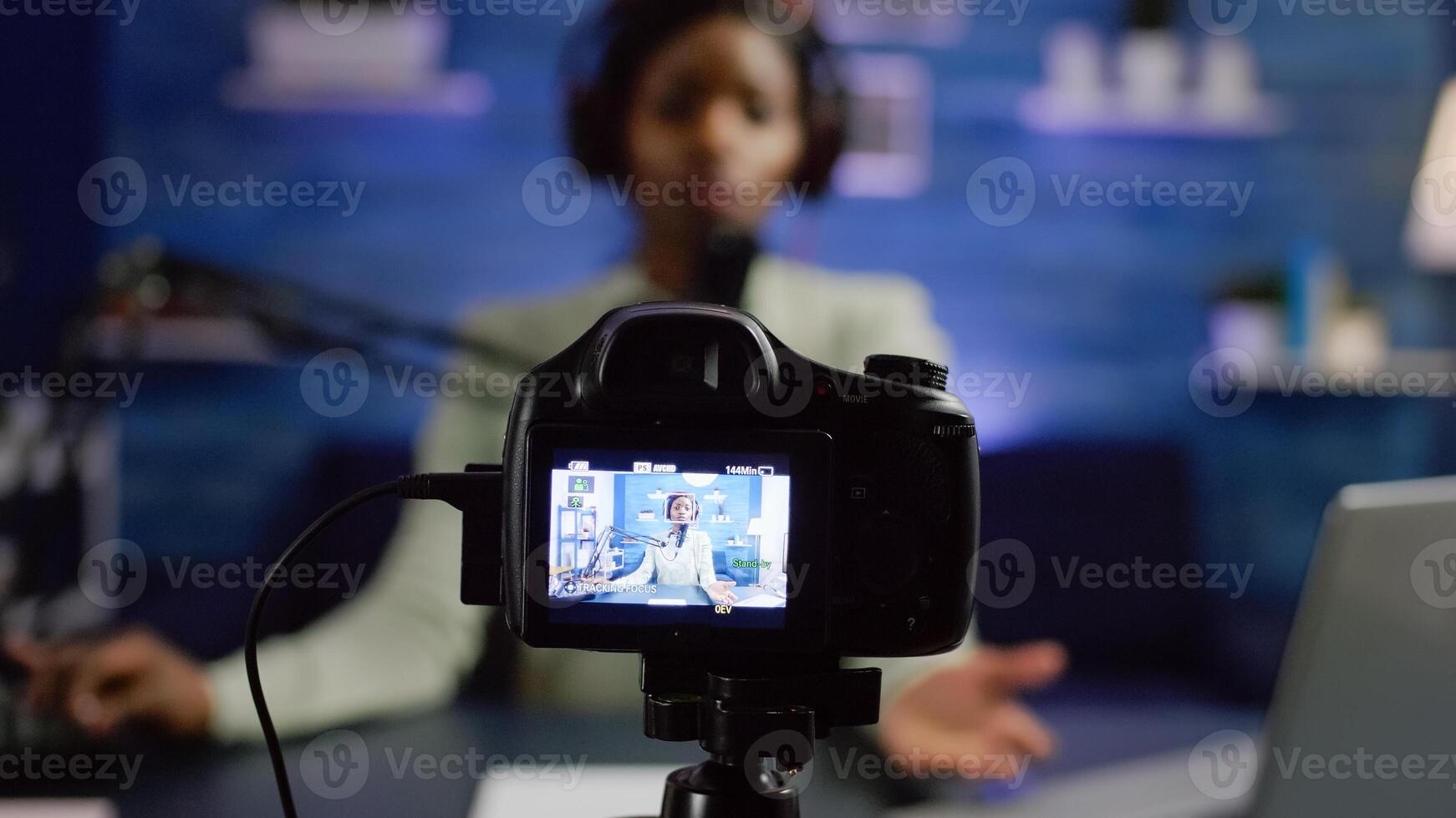 African influencer recording blog looking at professional camera at online talk show home studio. Social media content creator streaming online broadcast, blogger discussing wearing headphones. photo