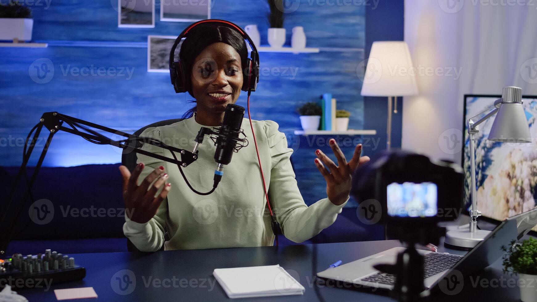 Black blogger influencer recording blog concept waving and speaking looking at camera on tripod in home podcast studio. Social media vlogger shooting vlog, streaming online broadcast photo