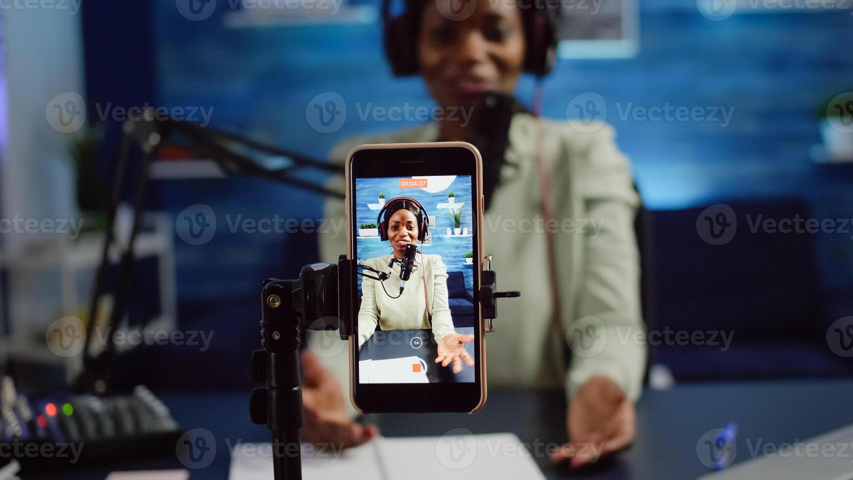 Close up of smartphone recording black woman influencer talking looking into it during online podcast. Social media content creator streaming online broadcast, blogger discussing wearing headphones. photo