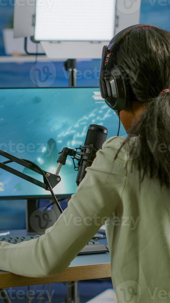 Black player wearing headphones talking with other players chatting while playing professional shooter games in online tournament. Gamer making online videogames with new graphics on powerful computer photo