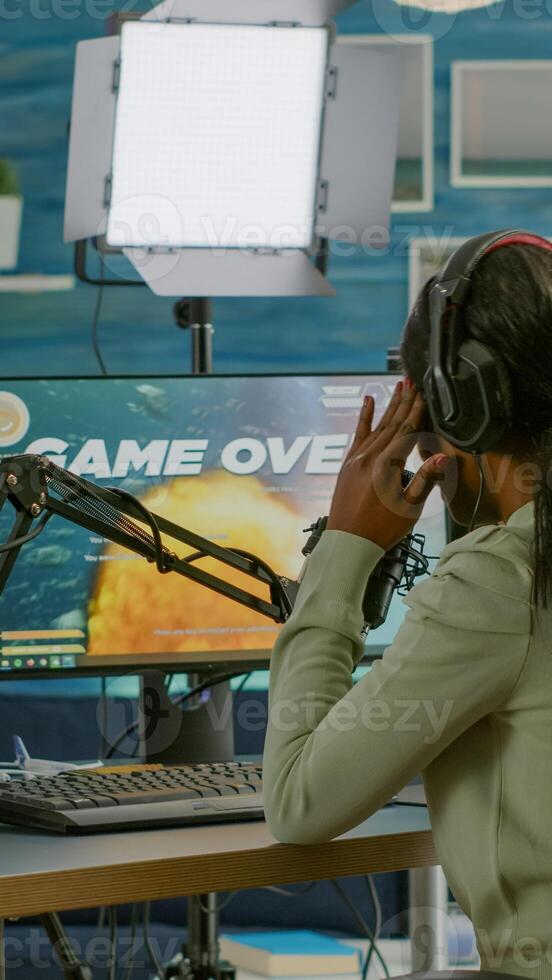 Afro streamer losing online championship being disappointed for space shooter game over. Pro gamer streaming online games with new graphics, talking on stream chat using RGB powerful computer. photo