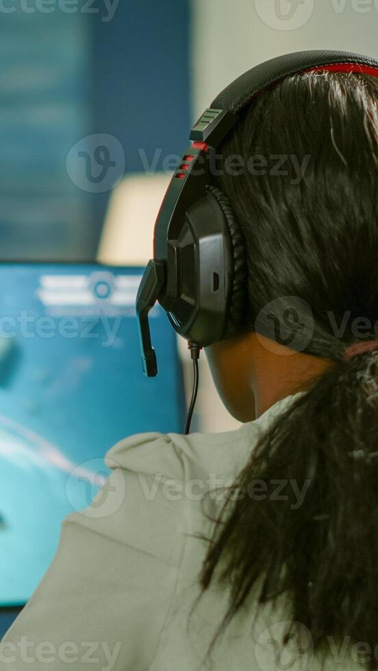Closeup of competitive black woman player holding joystick playing space shooter game at powerful computer late night. Professional gamer using wireless controller for online gaming championship photo