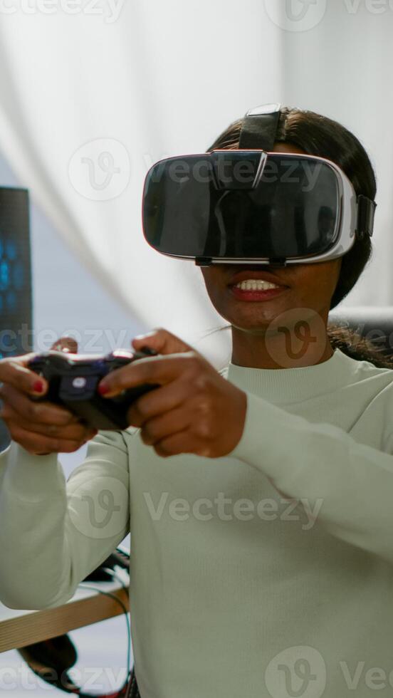 Black videogamer woman winning space shooter game using virtual reality goggles playing games with modern joypad. Professional gamer streaming online videogames with new graphics on powerful computer photo