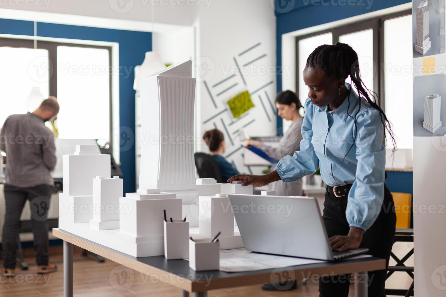 Architect african american woman working on laptop at workplace. Worker looking at building model maquette design for construction development. Modern urban layout project photo