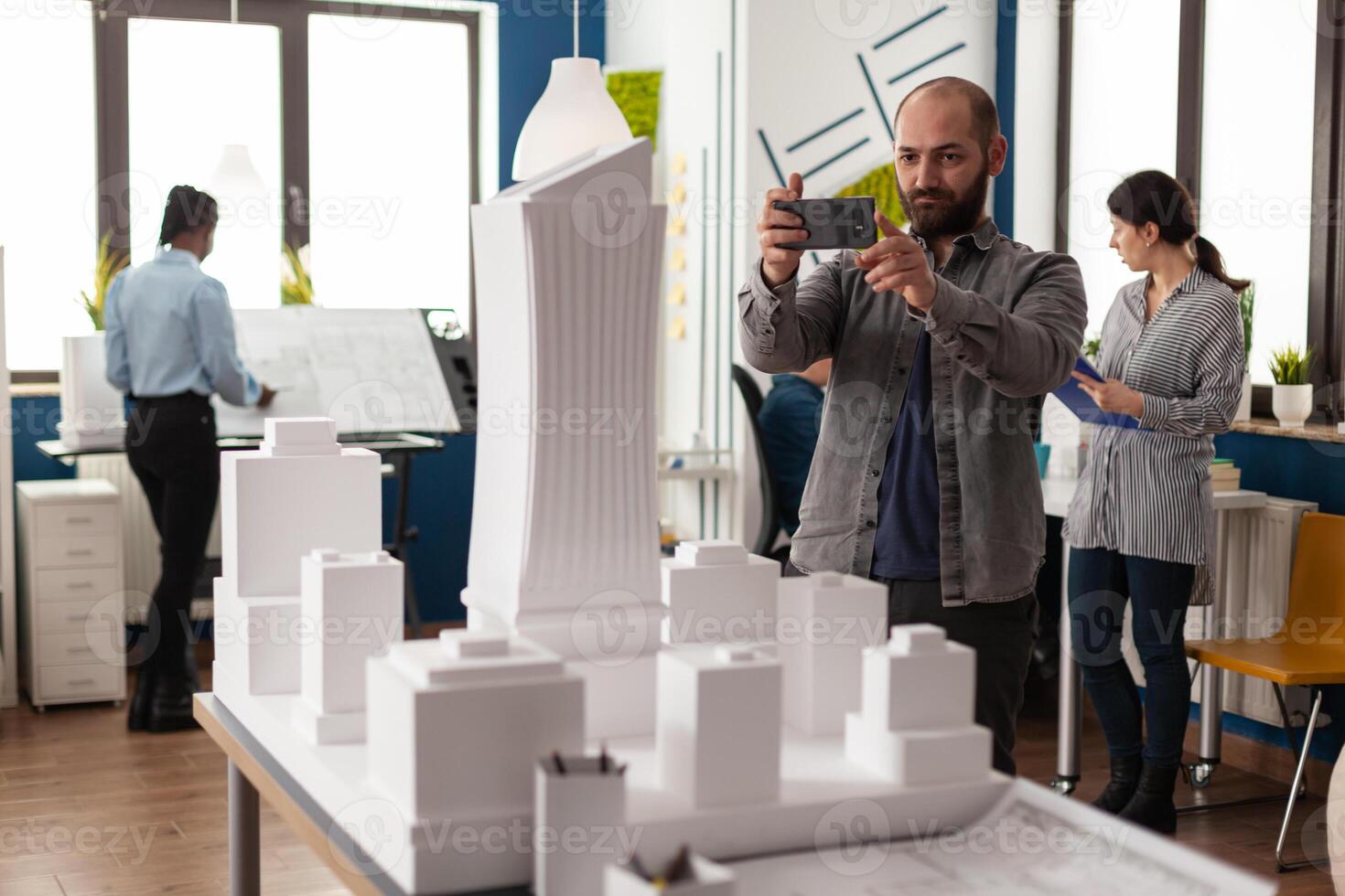 Architect profession man looking at maquette layout using smartphone to design building model plan maquette. Urban designer constructor working on professional modern construction photo