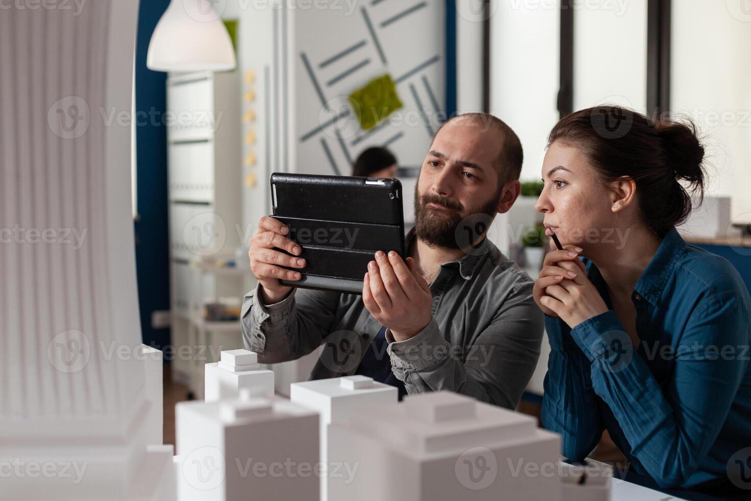 Design architecture colleagues sitting at office working on tablet and blueprints for layout plan maquette building model. Professional engineering team sitting for construction project photo