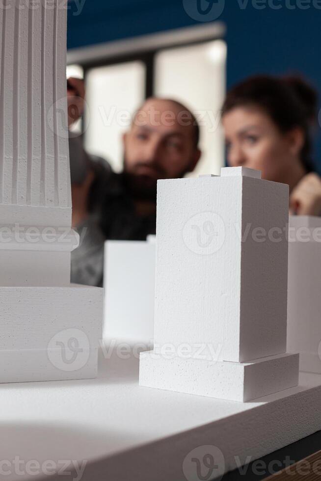 Talking architect team sitting at desk in professional office to work on building model maquette. Colleagues discussing plan of modern design architecture for layout project photo