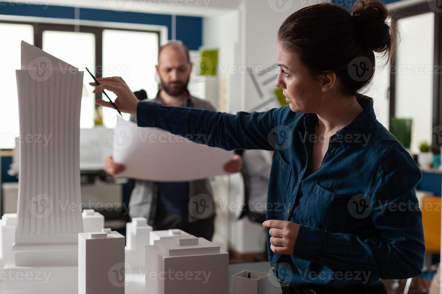 Architecture office partners looking at blueprints and plans for building model maquette. Caucasian professional workers pointing at construction design layout for urban project photo