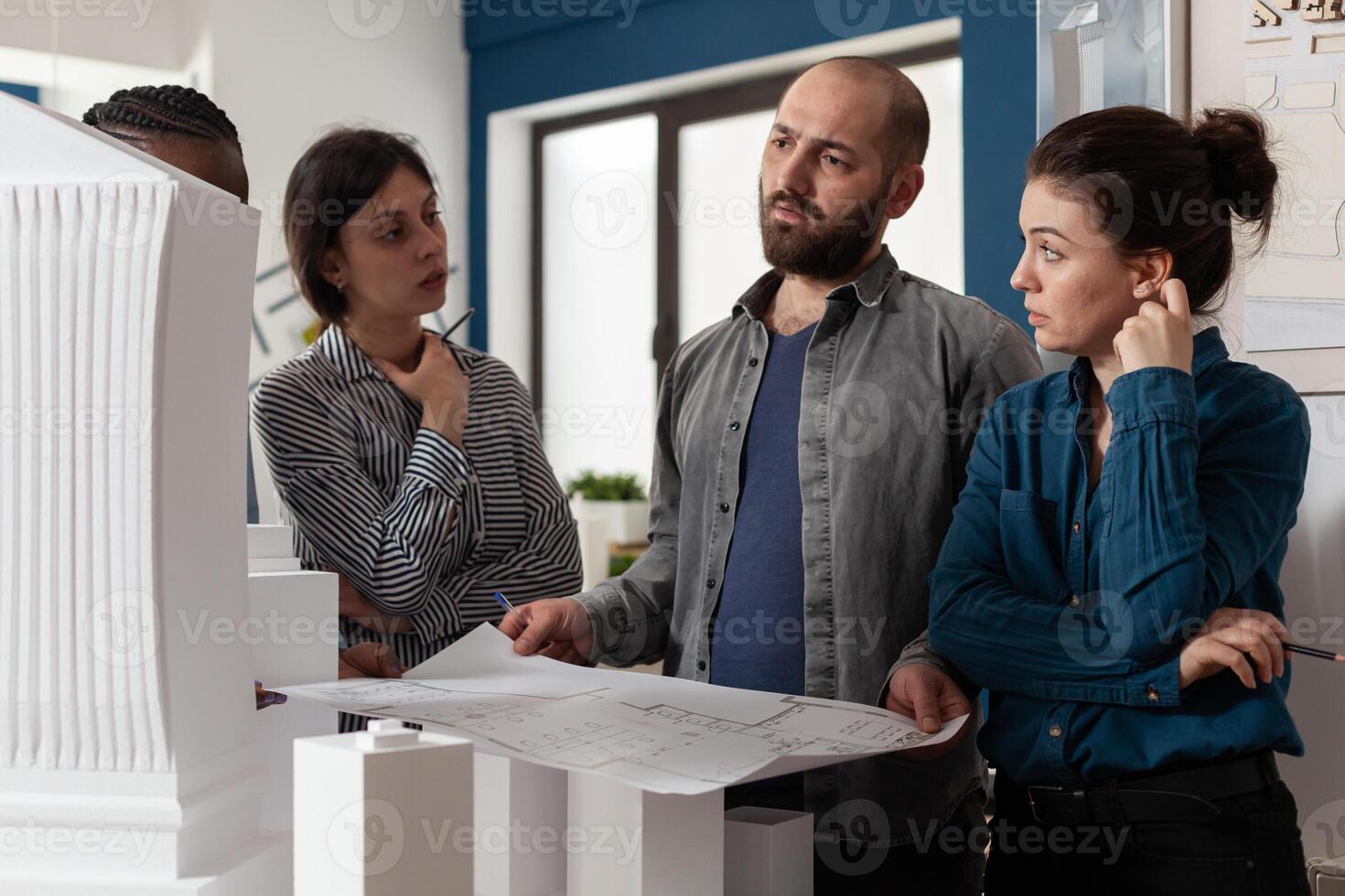 Architectural diverse work group talking about project design construction. Multi ethnic professional team working on maquette building model for engineering industry and business photo