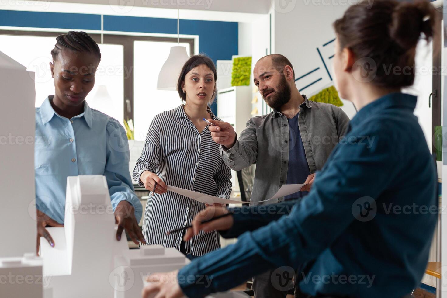 Architectural diverse work group talking about project design construction. Multi ethnic professional team working on maquette building model for engineering industry and business photo