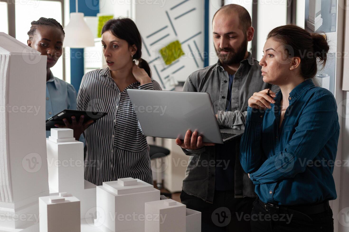 Architecture multi ethnic workers meeting at office analyzing blueprint plans on laptop computer tablet. Group working on maquette building model project design construction photo