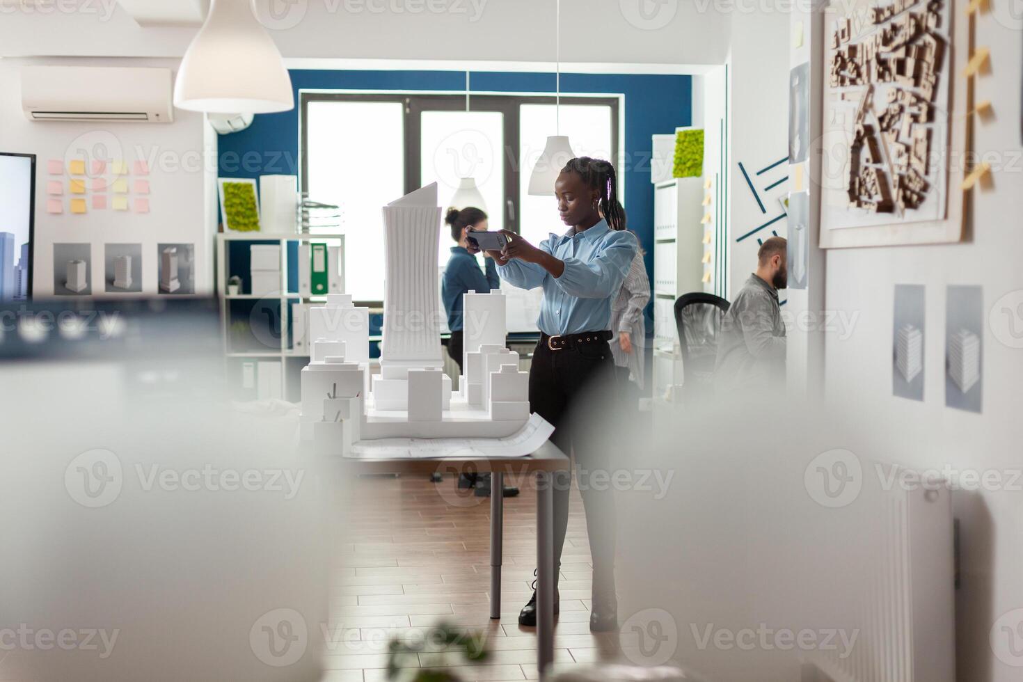 Architect working with smartphone to photograph maquette of skyscraper building complex. Engineer with mobile device next to table with white foam scale model in architectural modern office. photo
