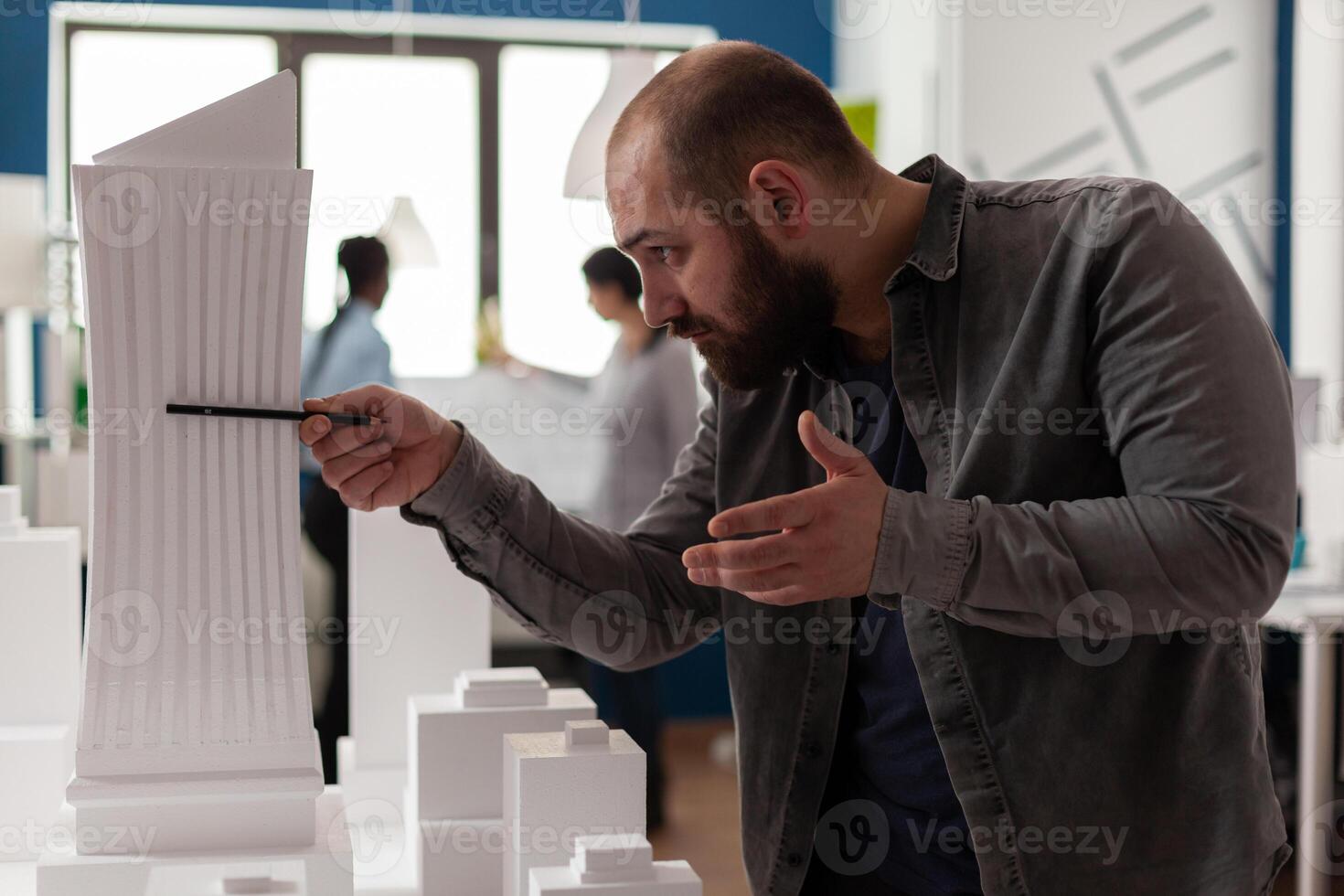 Engineer holding pen inspecting the design of skyscraper maquette in modern office. Inspired architect looking at the architectural lines of white foam model of residential project. photo