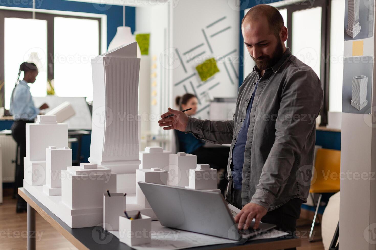 Arhitectural designer in videocall conference presenting white foam building model of residential buildings to client. Architect using laptop computer in modern office next to desk with 3d maquette. photo