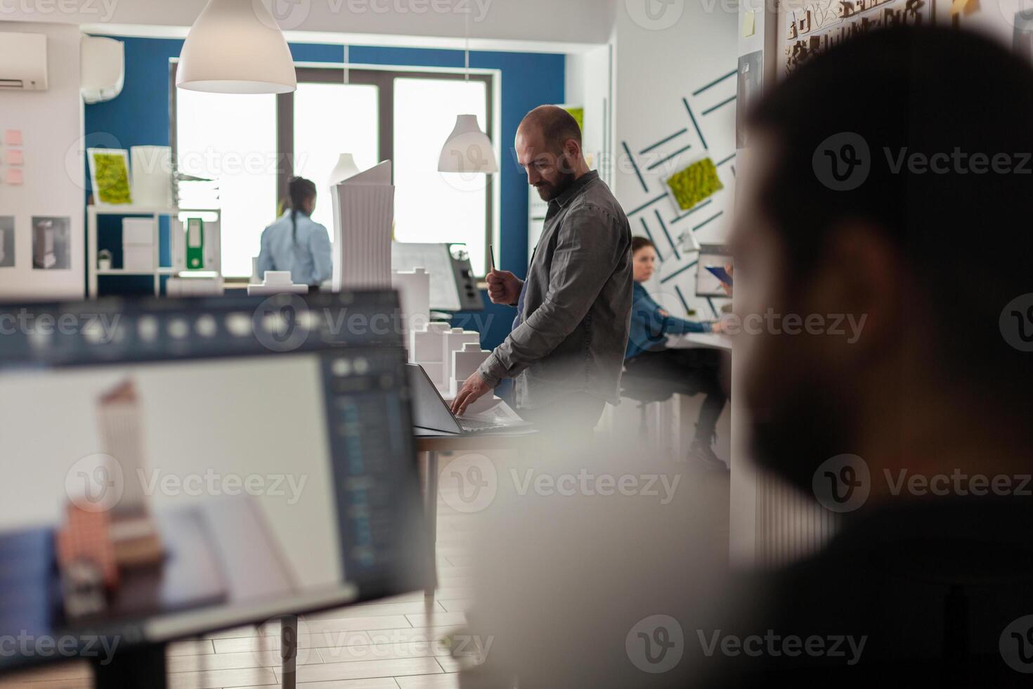 Engineer looking at blueprints on laptop at desk with architectural model of office buildings. Architect working with computer to create modern design concept of residential urban project. photo