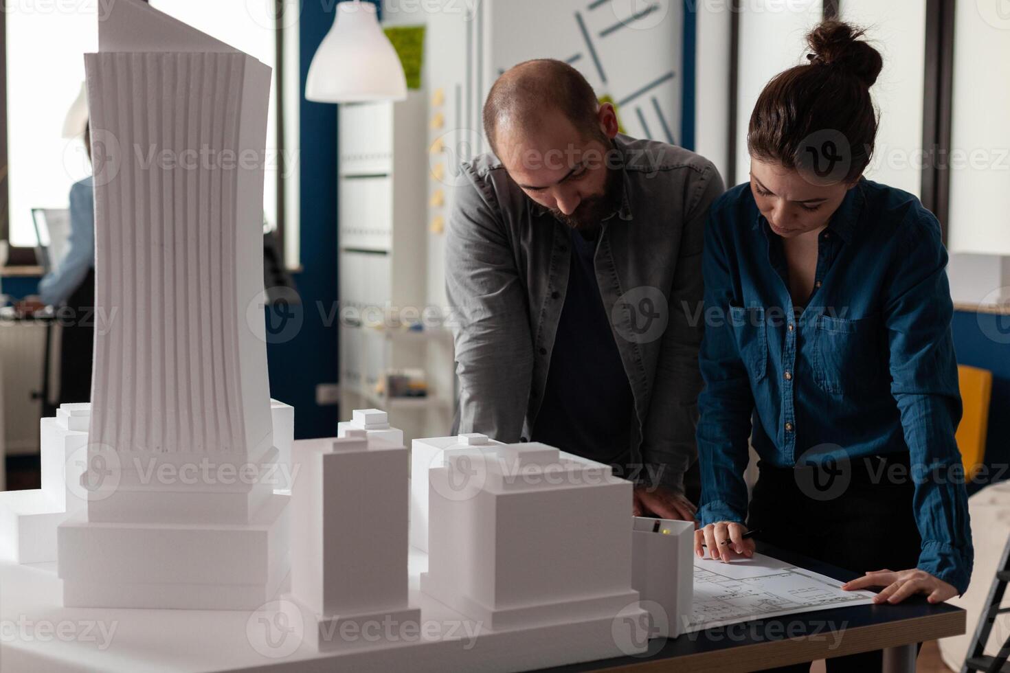 Team of two architects colleagues collaborating looking down at blueprints of urban planning project. Architectural engineers doing teamwork reading construction plans. photo