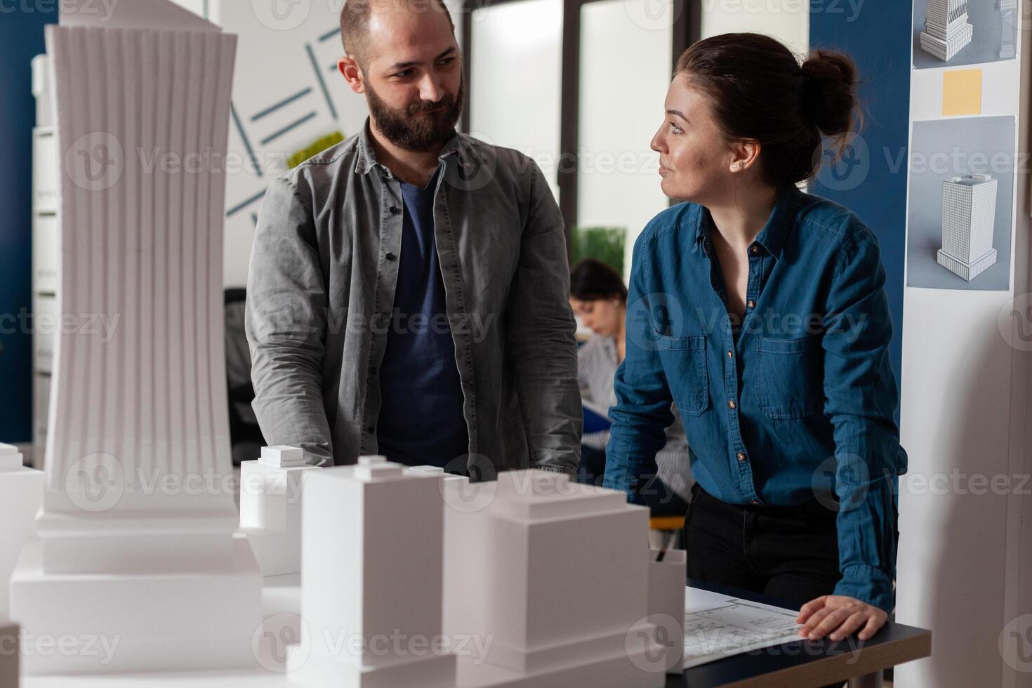 Architects doing teamwork looking at each other discussing blueprints in modern architecture office. Team of two architects colleagues working together at urban planning project. photo