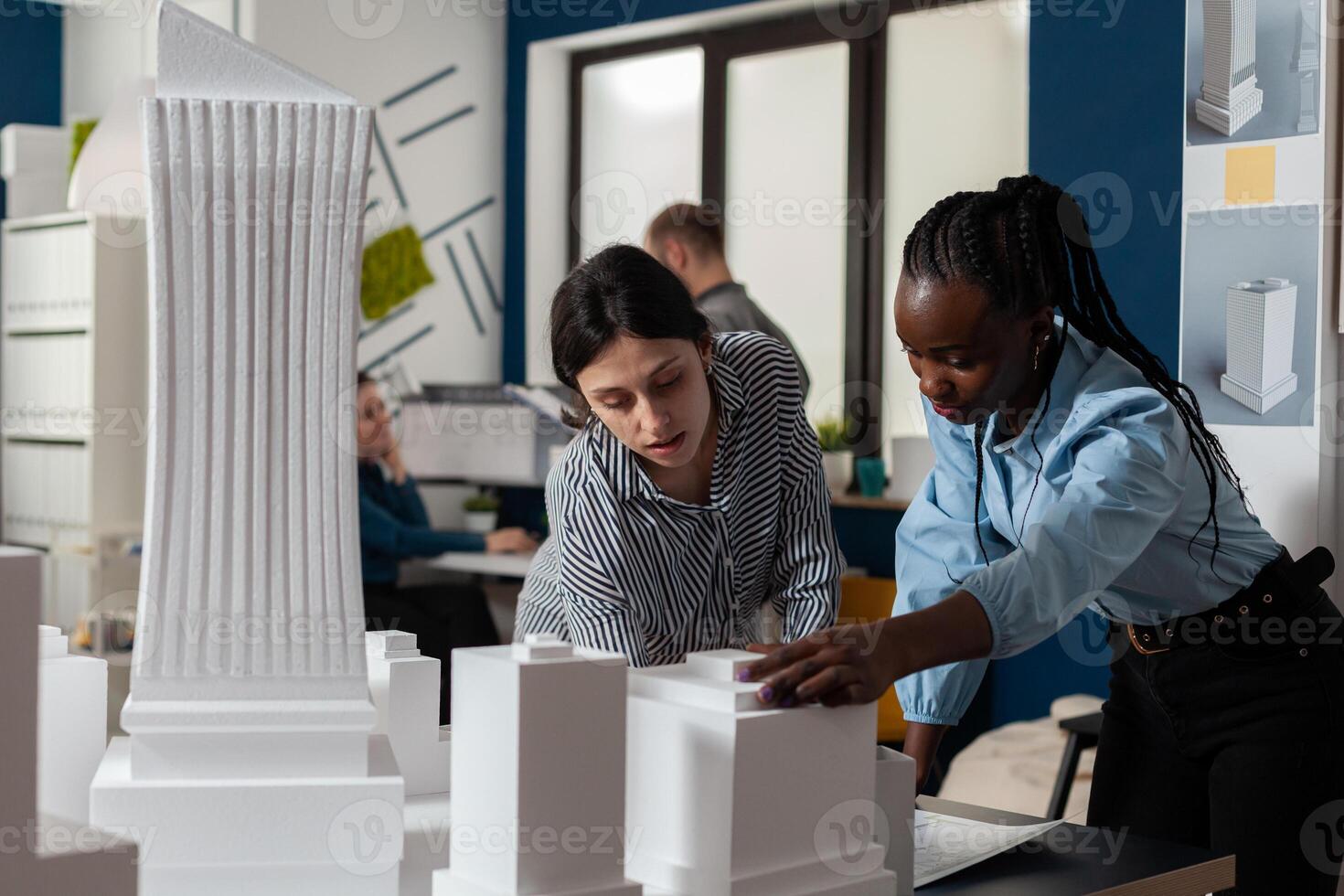 Architectural engineers doing teamwork reading construction plans over table with white foam scale model of buildings. Team of two architects colleagues collaborating looking down at blueprints. photo