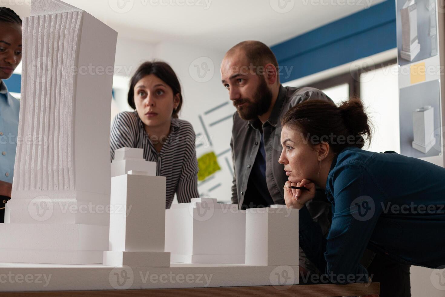 Team of professional architects looking at skyscraper maquette in architectural office. Engineer partners working on group project at desk with real estate construction model. photo