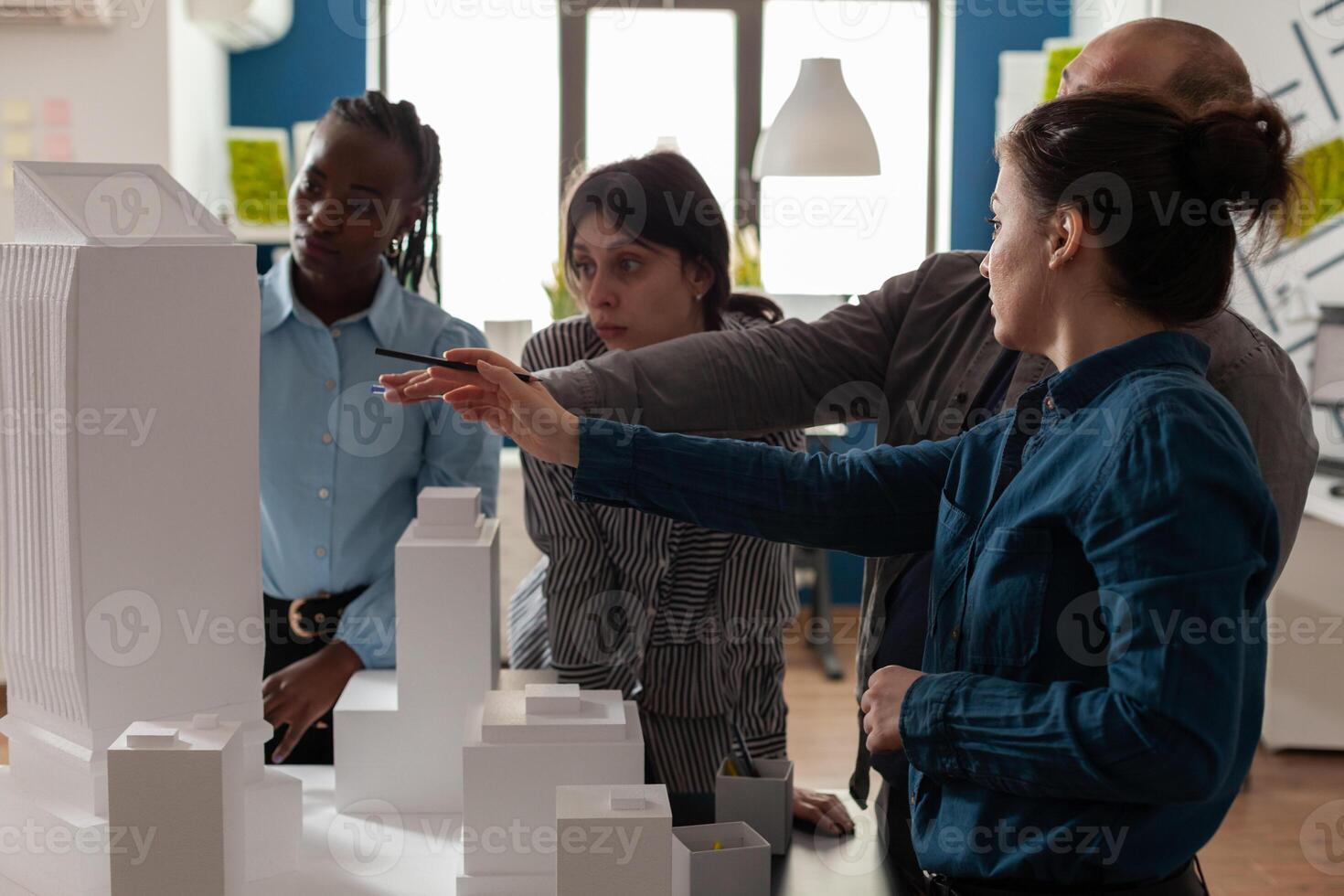 Team of professional architects brainstorming ideeas pointing at real estate construction model in architectural office. Mixed group of engineers working on residential project at desk. photo