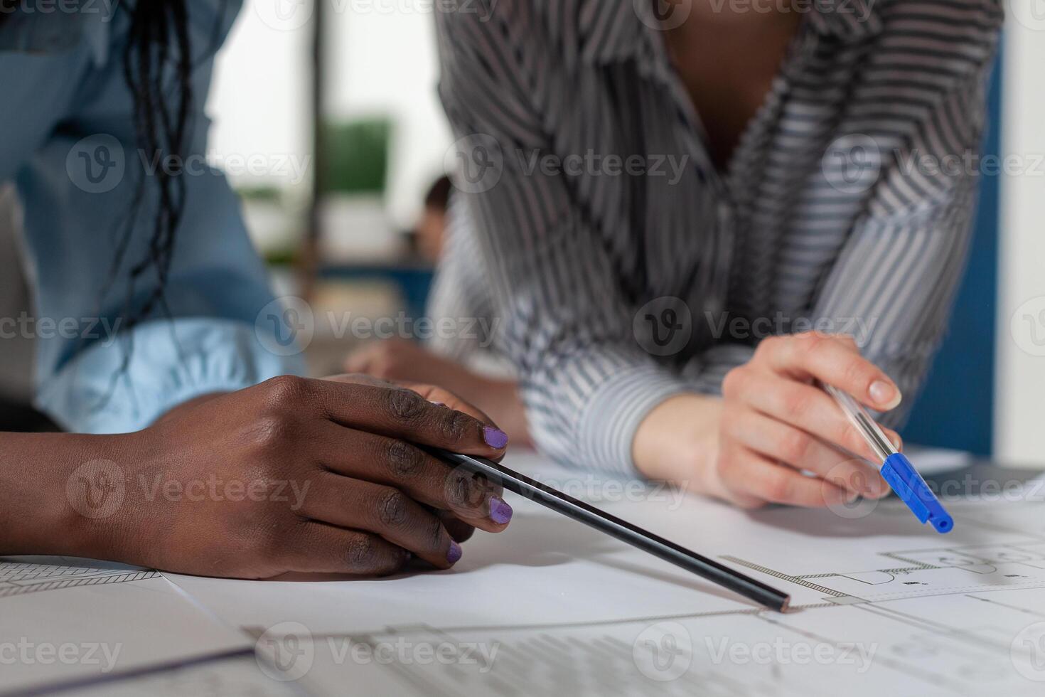 Closeup of architectural engineer hands holding pencil and pen over blueprints at modern technical drawing desk. Detailed view of architects inspecting construction plans of residential project. photo