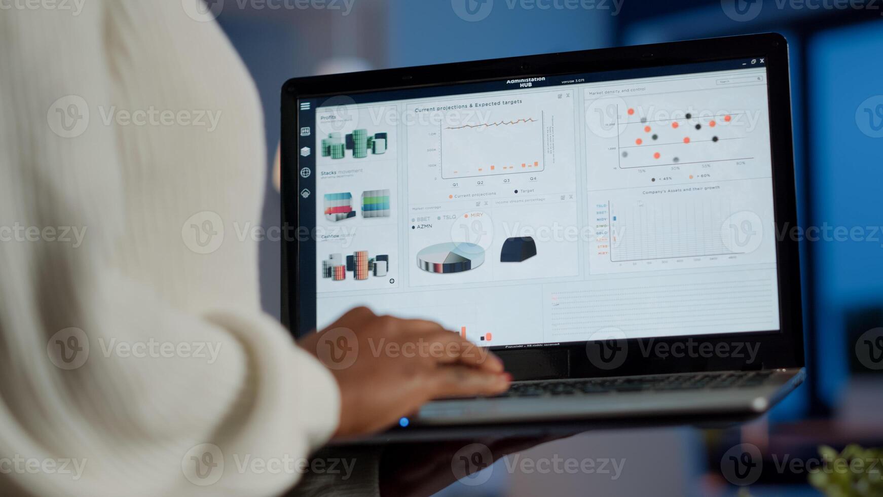 Back view of african business woman analysing financial statistics holding laptop standing in start-up office overworking. Busy focused employee using modern technology network wireless overtime photo