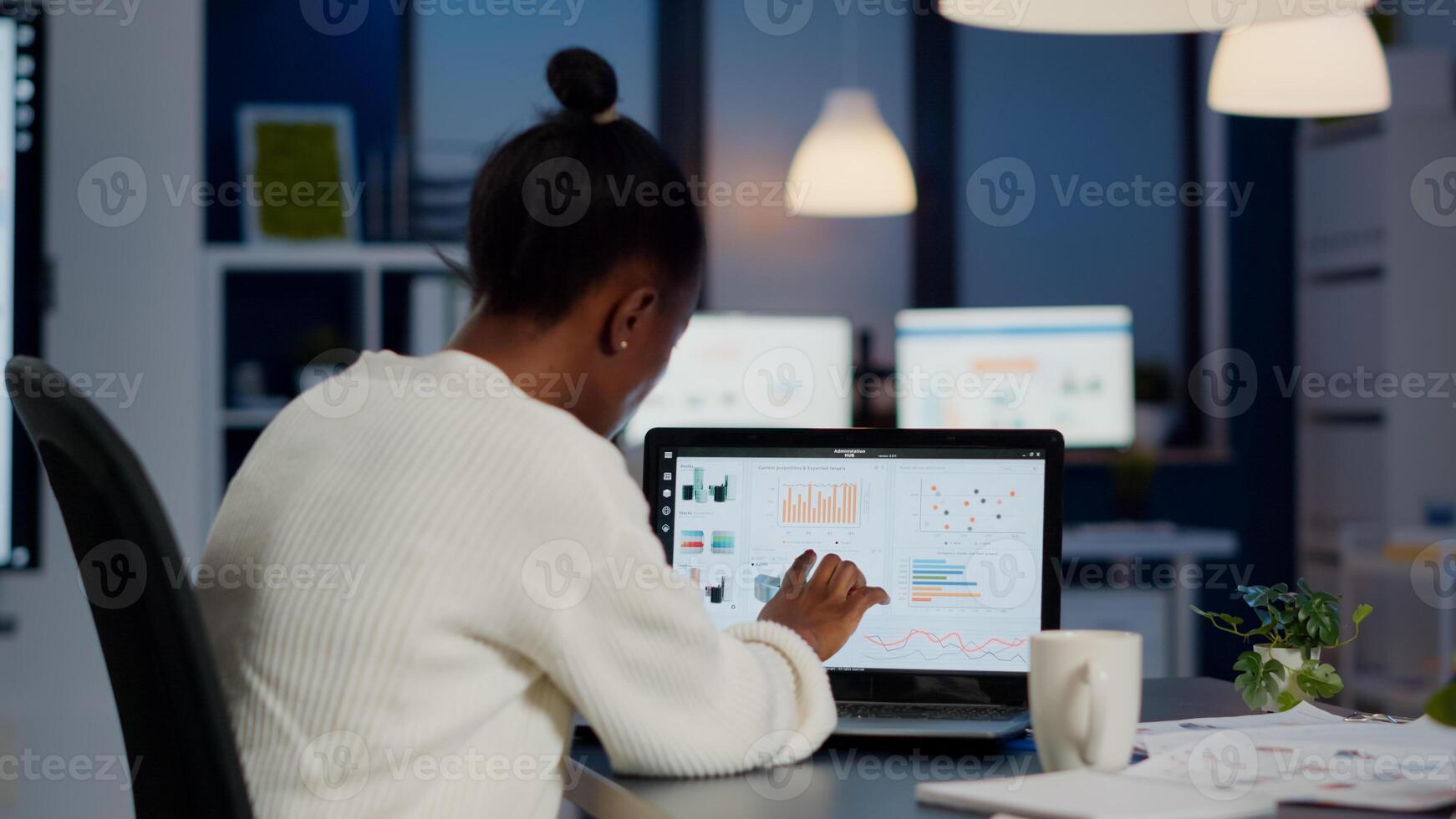 Black woman manager checking business statistics and financial reports on laptop working in start up office late at night. Focused employee doing overtime for job respecting deadline of project photo