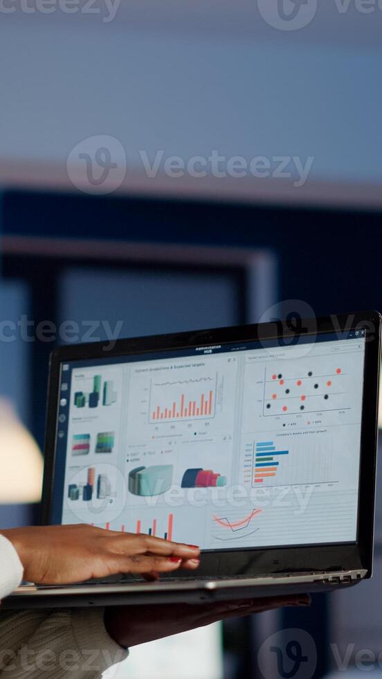 African freelancer typing on laptop late at night standing in start up business office late at night working. Busy employee using modern technology network wireless doing overtime for job searching photo