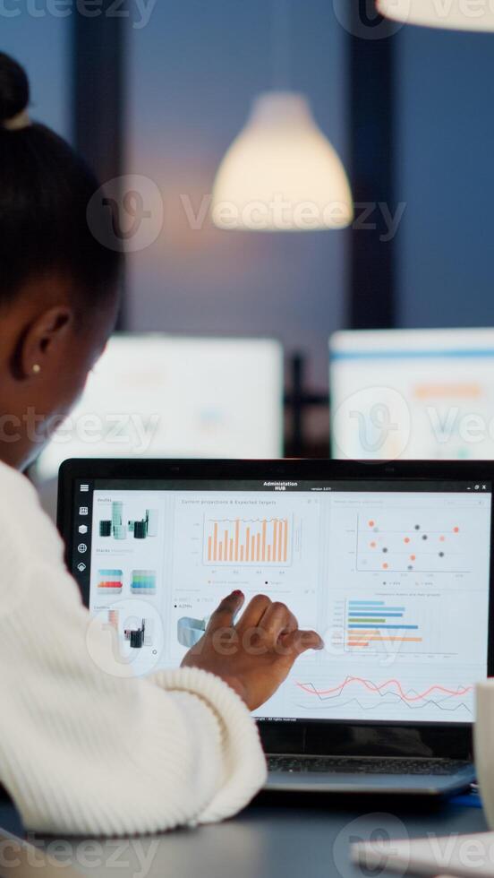 Black woman manager checking business statistics and financial reports on laptop working in start up office late at night. Focused employee doing overtime for job respecting deadline of project photo