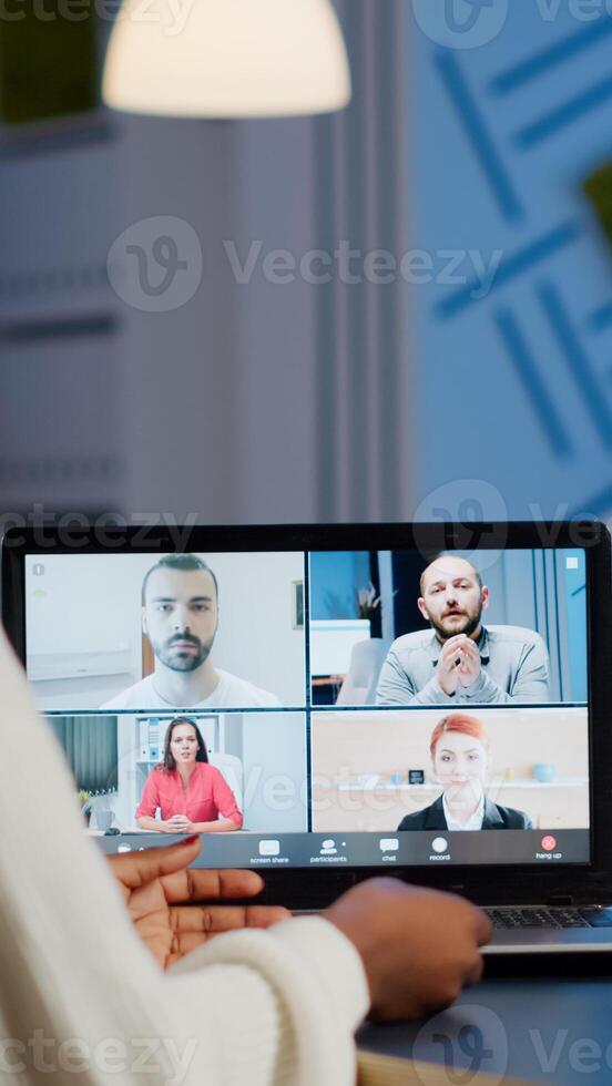 Back view of black business woman talking about sale report in conference working overtime in start-up office. Team using online wireless communication discussing on webcam during group meeting. photo