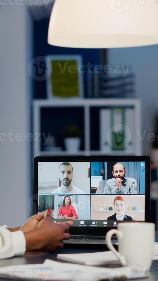 African businesswoman talking during conference with team in midnight using laptop in start up business office. Diverse workers talking during corporate meeting using technology network wireless photo