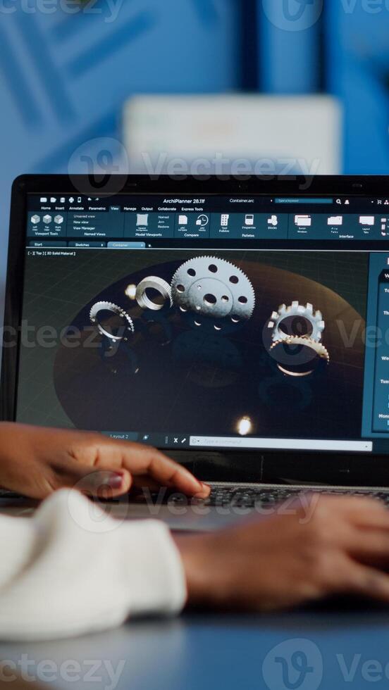 Tired african designer engineer analyzing new prototype of 3D model of industry product, working overtime. Industrial female worker studying gears idea on laptop showing cad software on device display photo