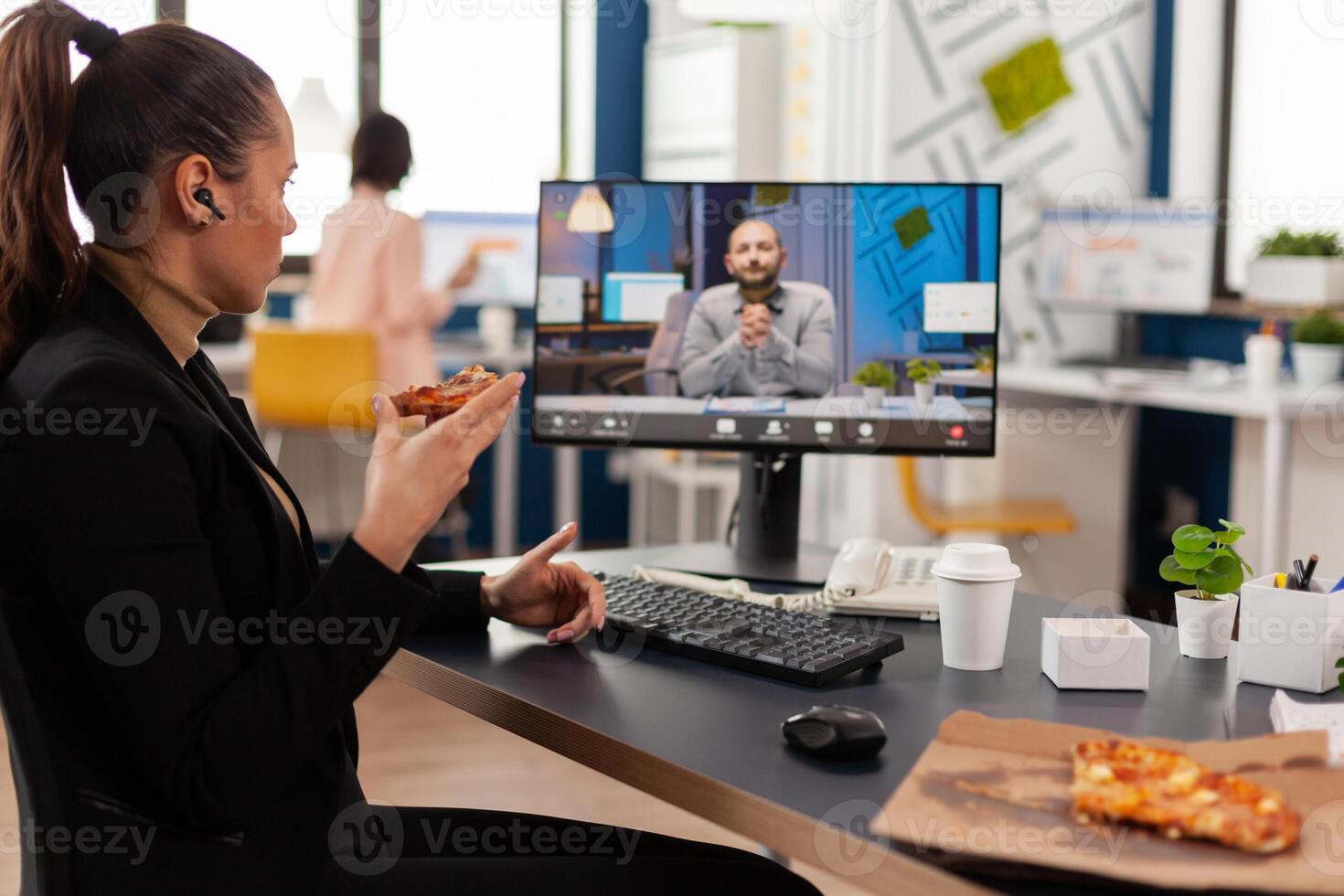 Businesswoman having delivery takeaway lunch meal order during takeout lunchtime at desk during online videocall meeting conference with remote manager. Entrepreneur eating pizza at workplace photo