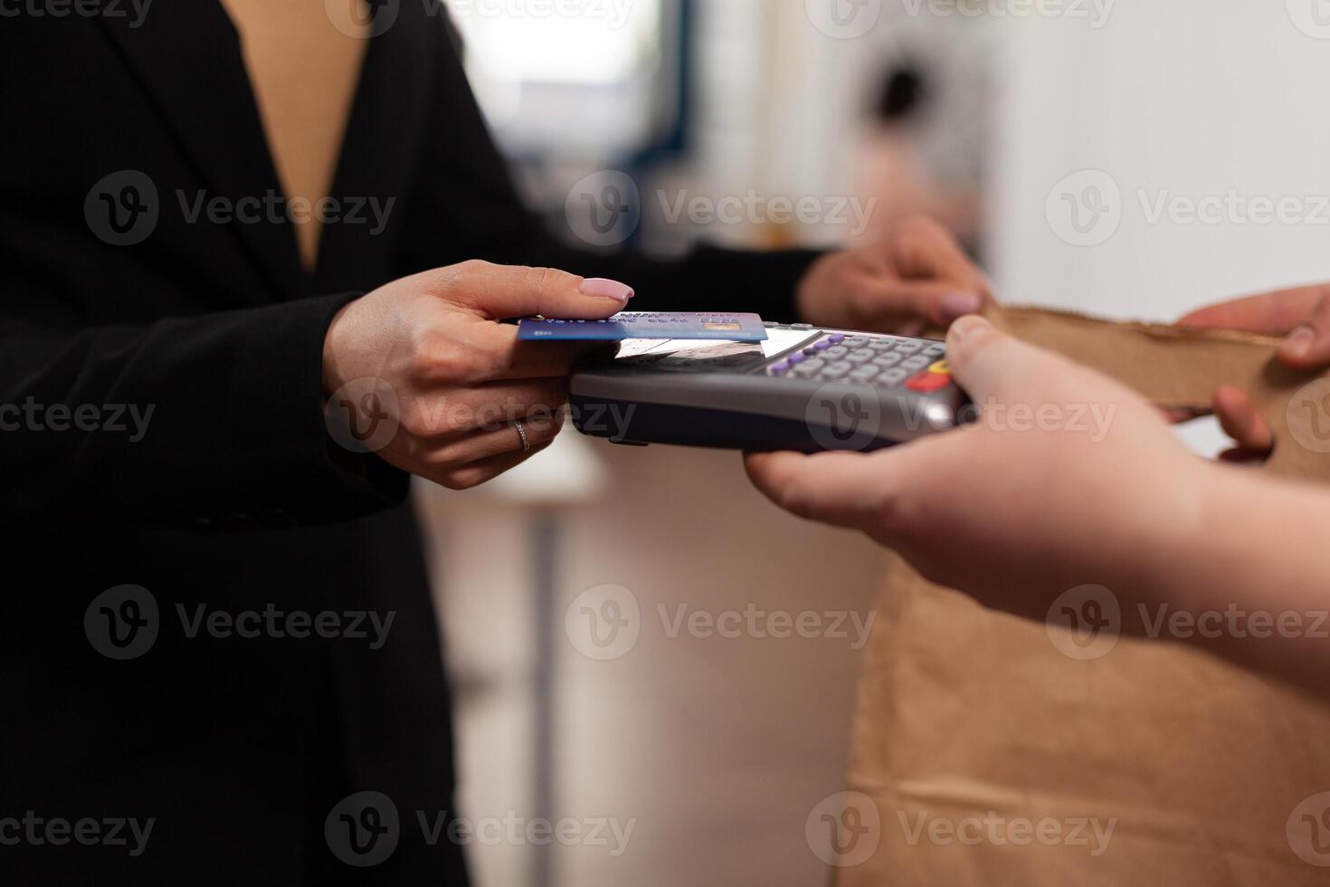 Close up of business woman holding credit card of pos, using contactless technology. Customer paying for their order with a credit card. Holding takeaway food in paper bag. photo