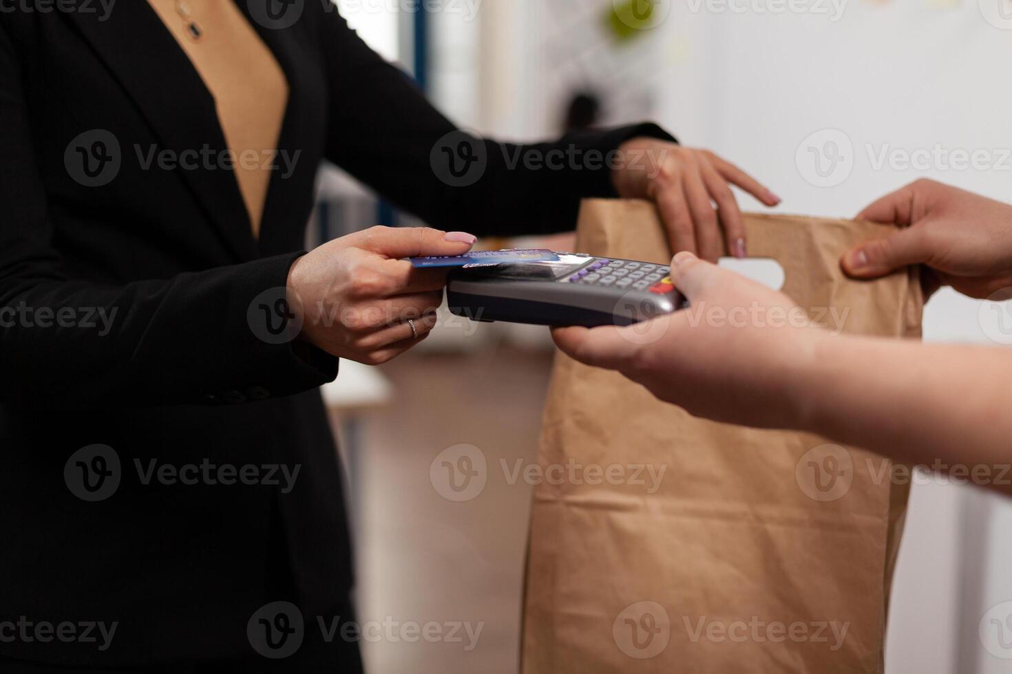Close up of business woman holding credit card of pos, using contactless technology, pay for takeaway food from courier. Holding box with meal lunch in paper bag. photo
