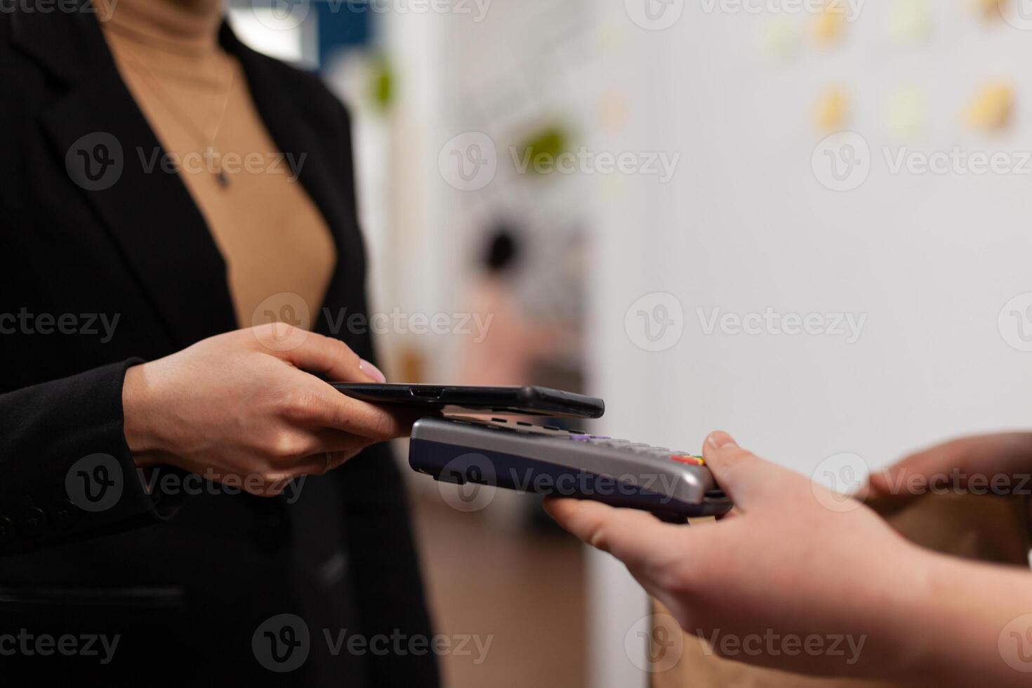 Close up of business woman paying delivery guy from frood service, using smartphone nfc technology. Entrepreneur recieving tasty takeaway lunch in paper bag. photo