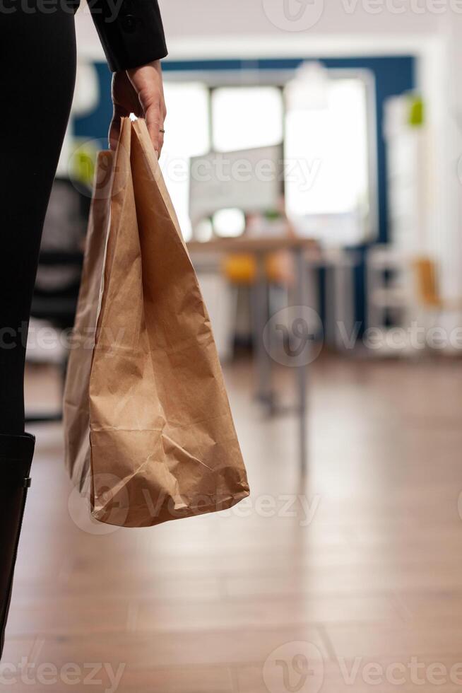 Businesswoman holding paper bag with takeaway food meal order putting on desk during takeout lunchtime in company office. Delivery man delivering fastfood packet for businesspeople. photo