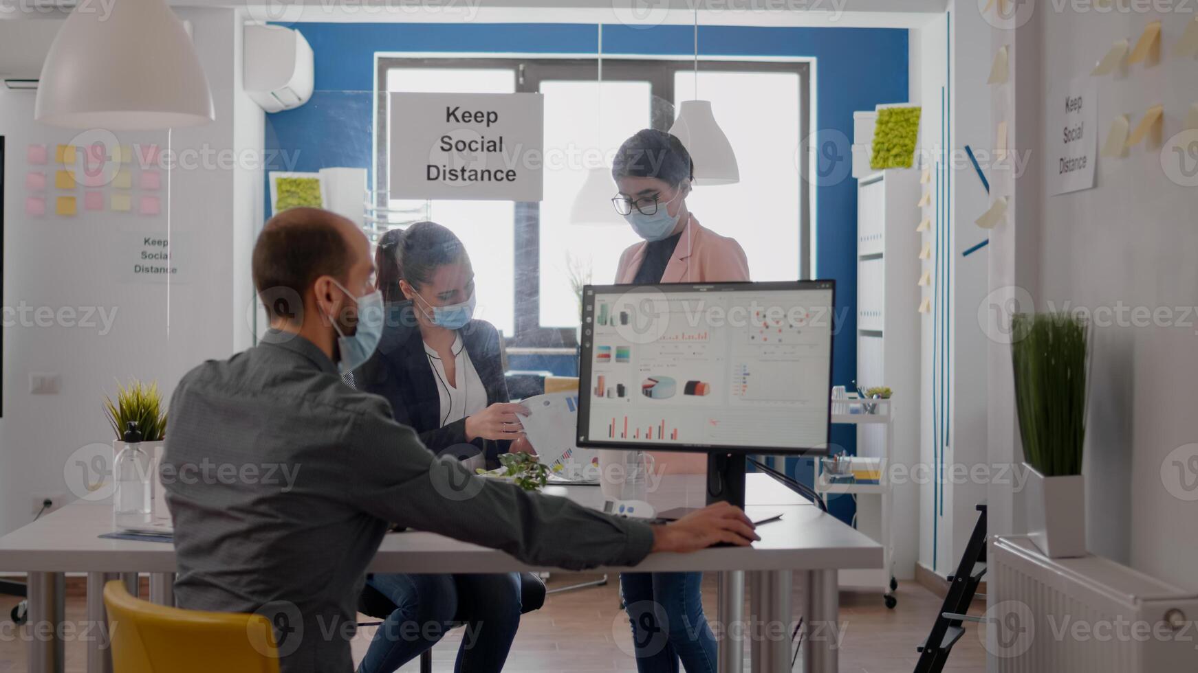 Teamworkers wearing protective medical face mask working at marketing project analysing reports while maintain social distancing in new normal office during covid19 global pandemic photo