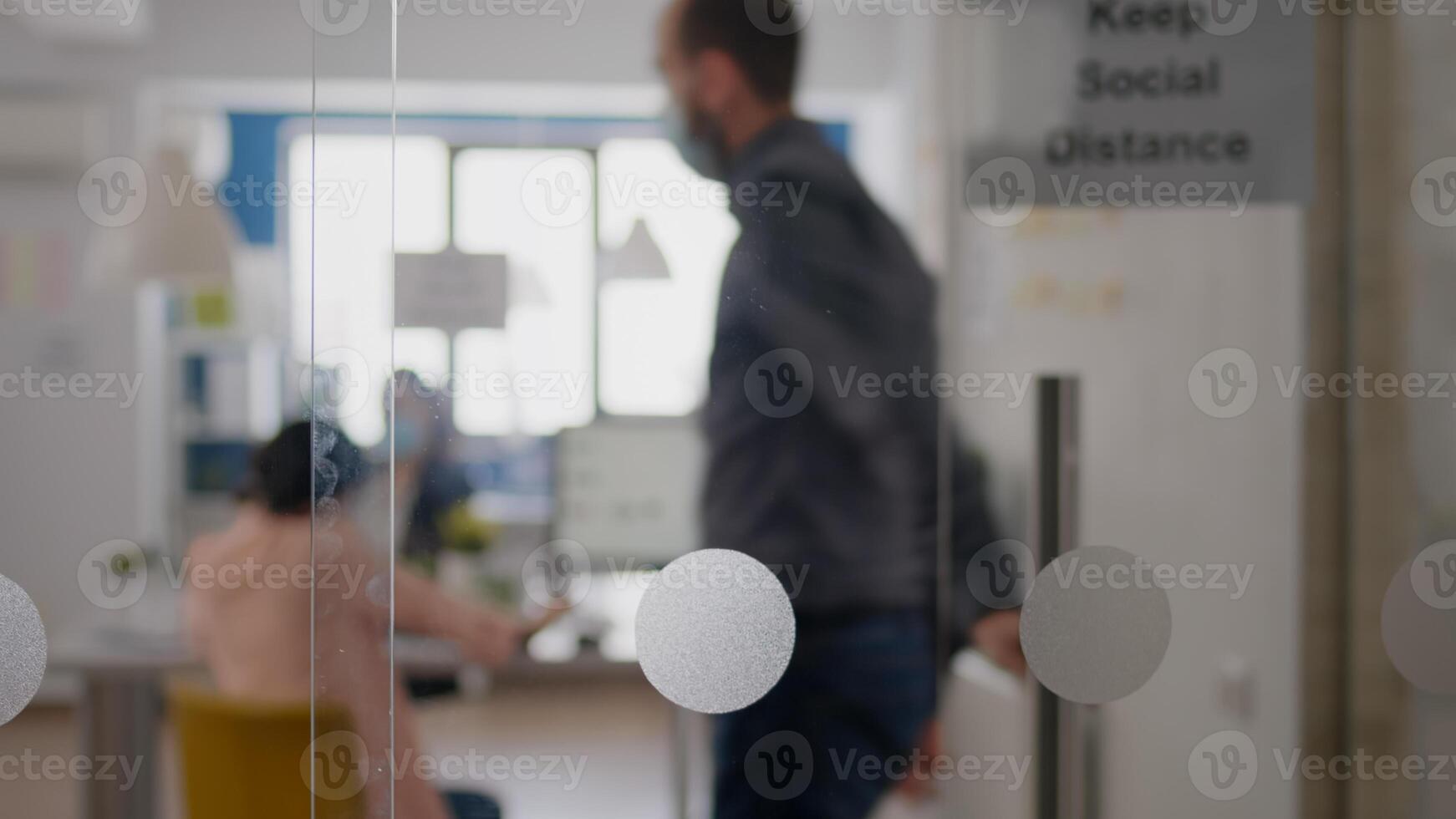 Woman with protective medical face mask talking on phone while coworkers working on computer, respecting social distancing in startup business office to avoid infection with coronavirus photo