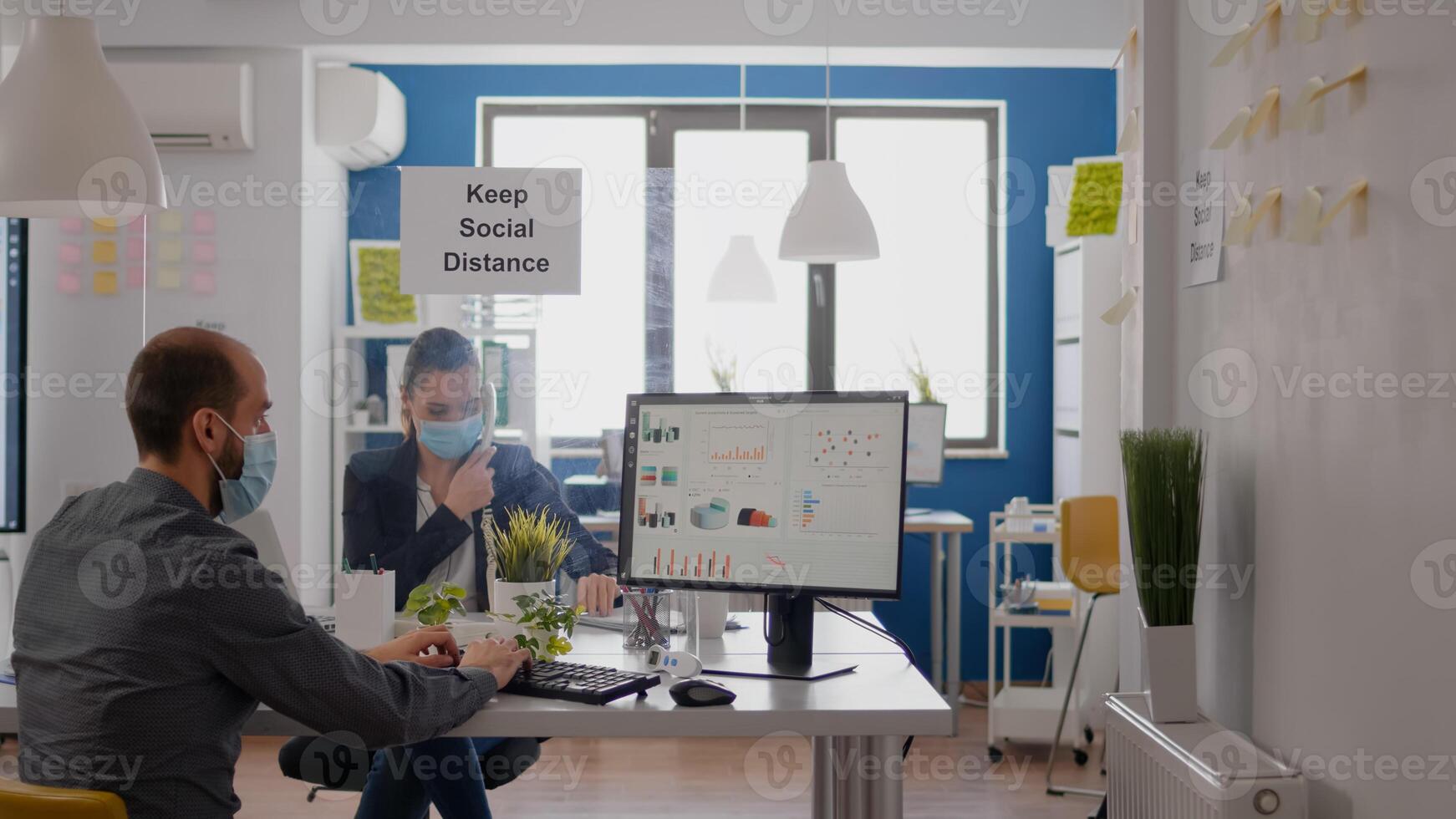Freelancer with protection medical face mask working on laptop computer while talking on phone with team. Businesswoman sitting at desk table in new normal company office during covid19 quarantine photo