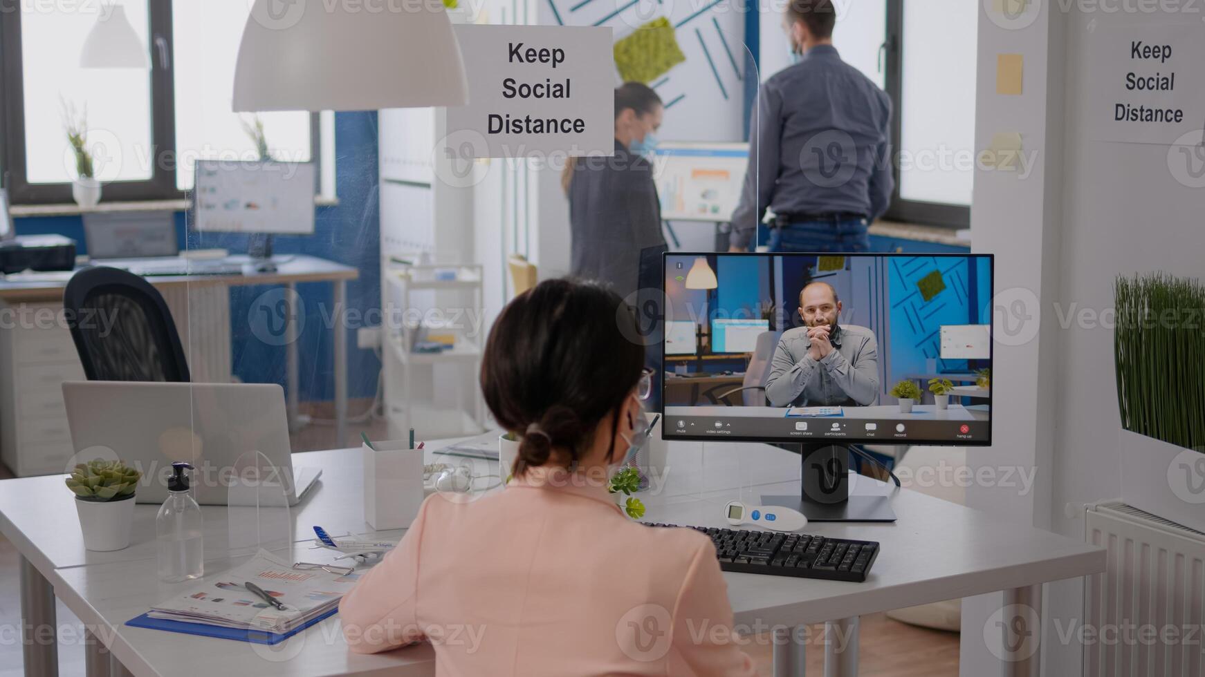 Freelancer sitting at desk table in new normal company office, wearing protection face mask during virtual videocall conference. Coworkers working on computer during coronavirus pandemic photo