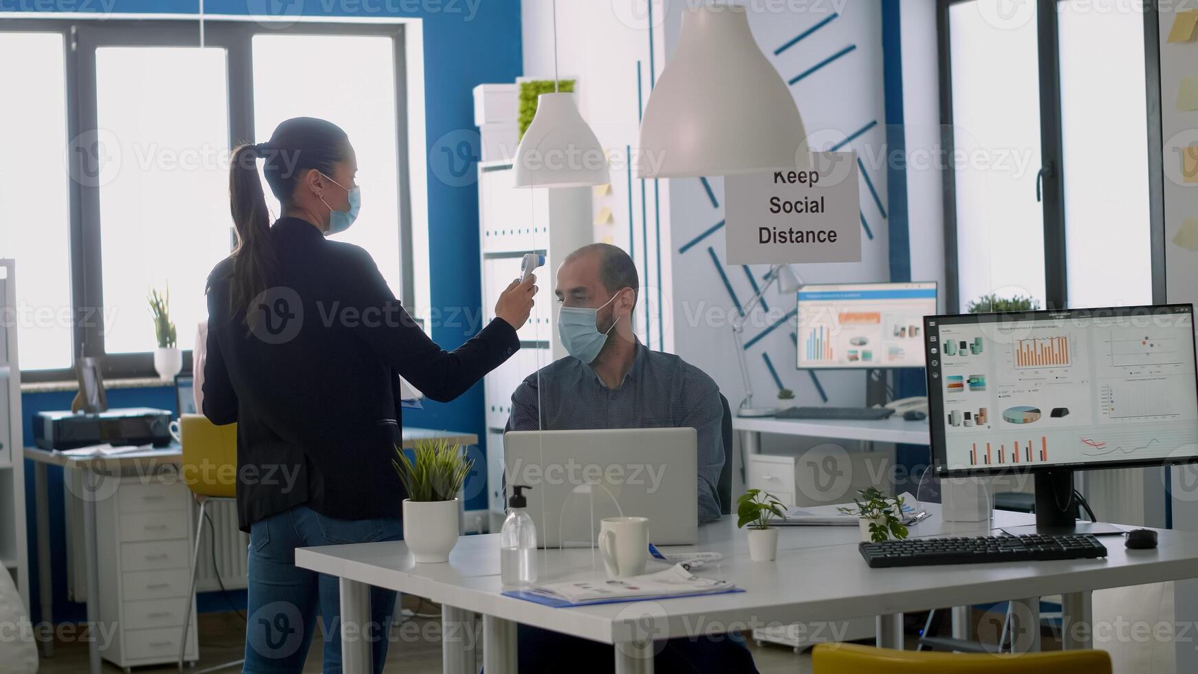 Business woman with protective face mask checking team temperature using medical thermometer. Coworkers respecting social distance in new normal company office to avoid infection with virus disease photo