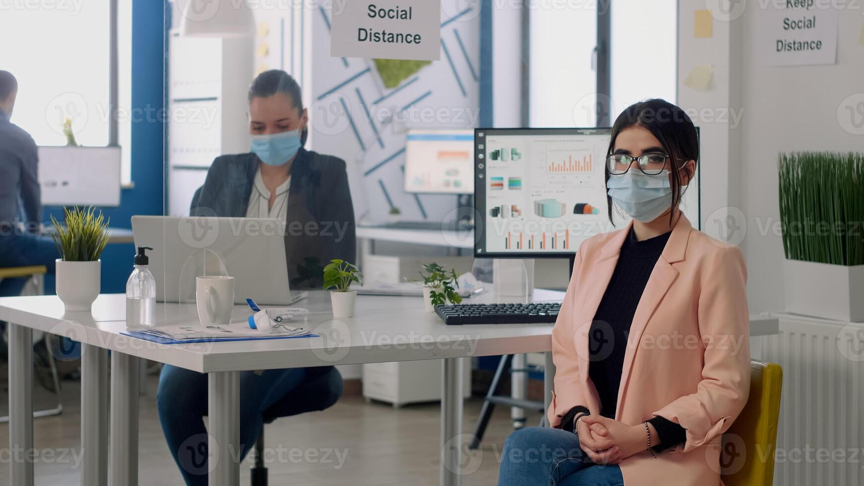 Portrait of manager with face mask sitting on chair at desk table in nre normal business company office. Teamworkers working in background respecting social distancing during coronavirus pandemic photo