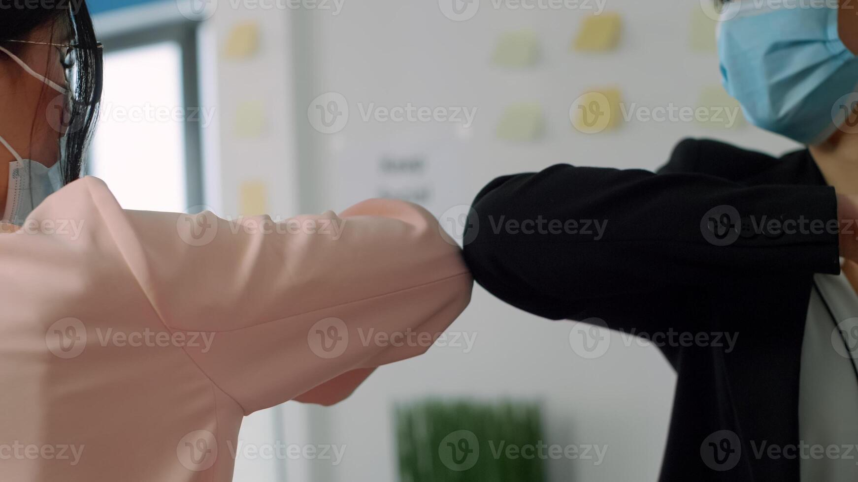 Closeup of two collegue wearing protective medical face masks touching elbow during coronavirus epidemic. Coworkers respecting social distancing while working in business office photo