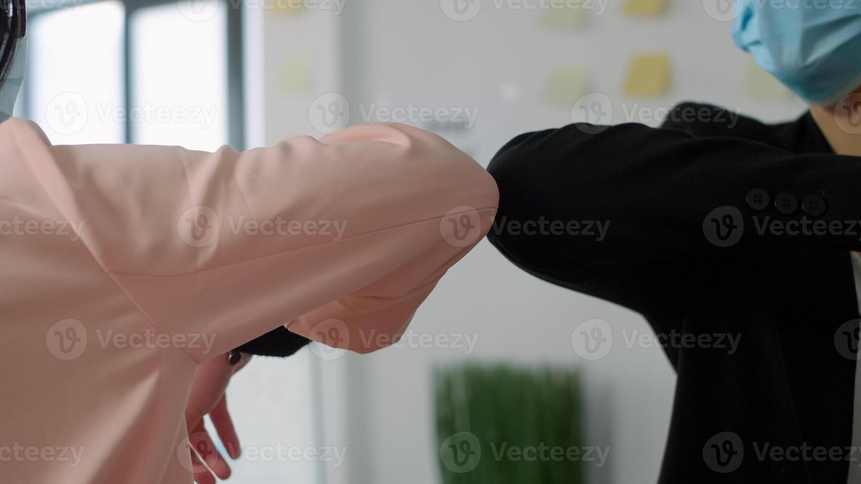 Closeup of colleagues with medical face masks greeting with elbow while working in company office. Coworkers keeping social distancing to avoid infection with coronavirus during covid19 lockdown photo