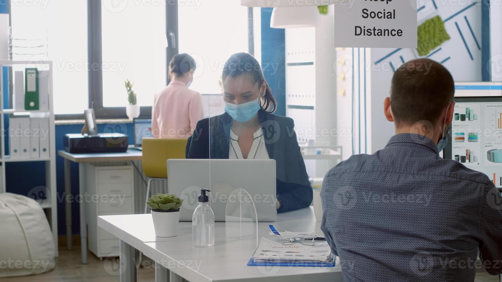 Business team with face masks working in company office taking precaution to mantain safety measures to avoid coronavirus infection. Collegues respecting social distancing during covid19 quarantine photo