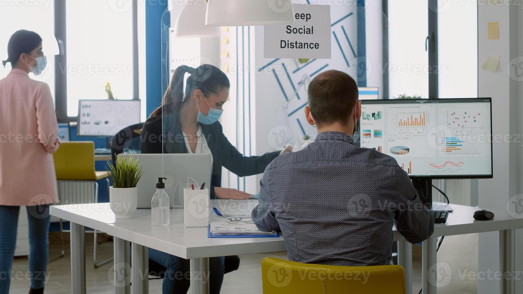 Teamworkers wearing face masks while working at marketing project using computer sitting at table desk in business company office. Coworkers keeping social distancing to avoid infection with covid19 photo