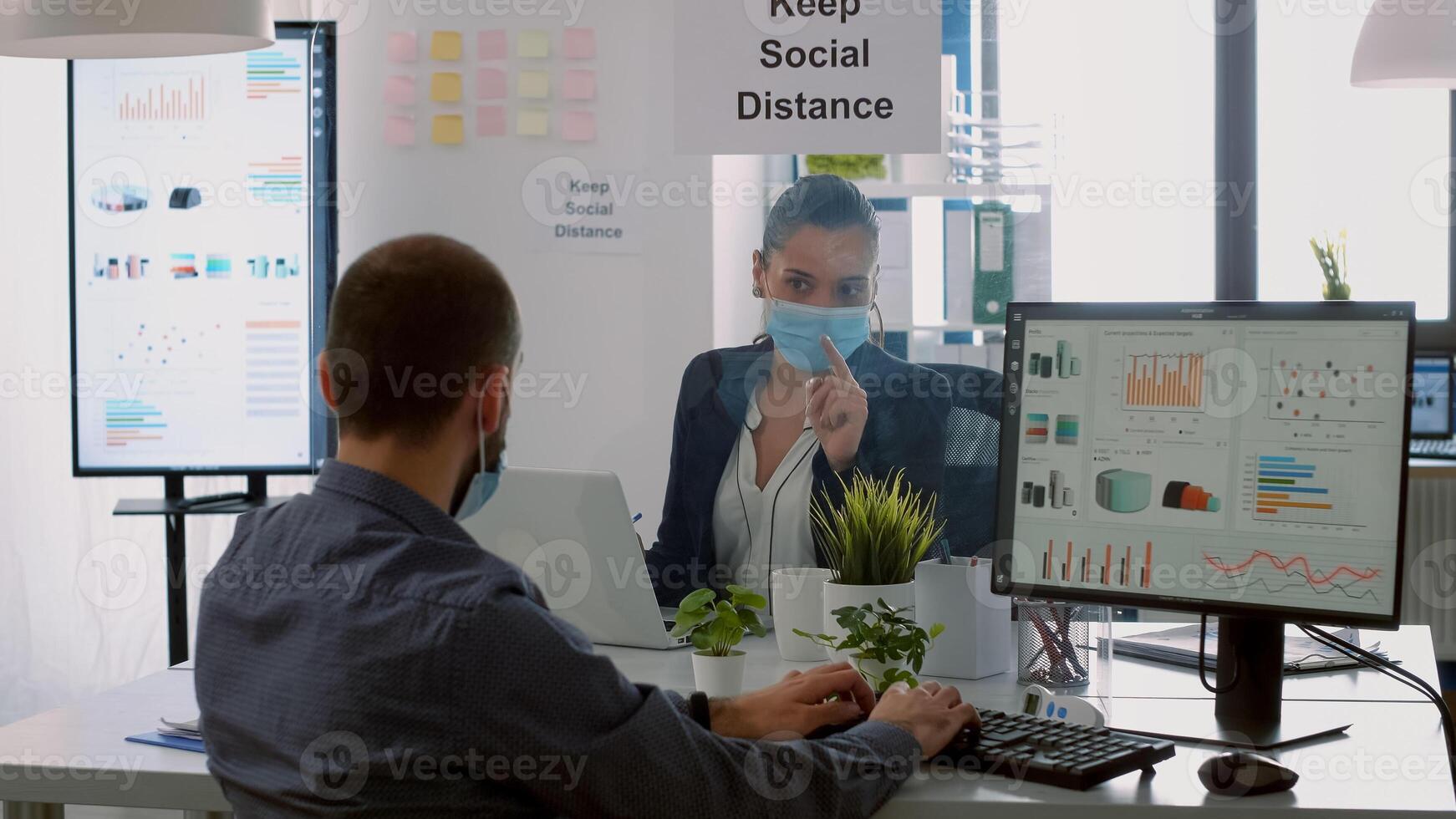 Business team with protection face masks working together in company office during corona virus global pandemic. Coworkers keeping social distancing while typing on computer checking reports photo