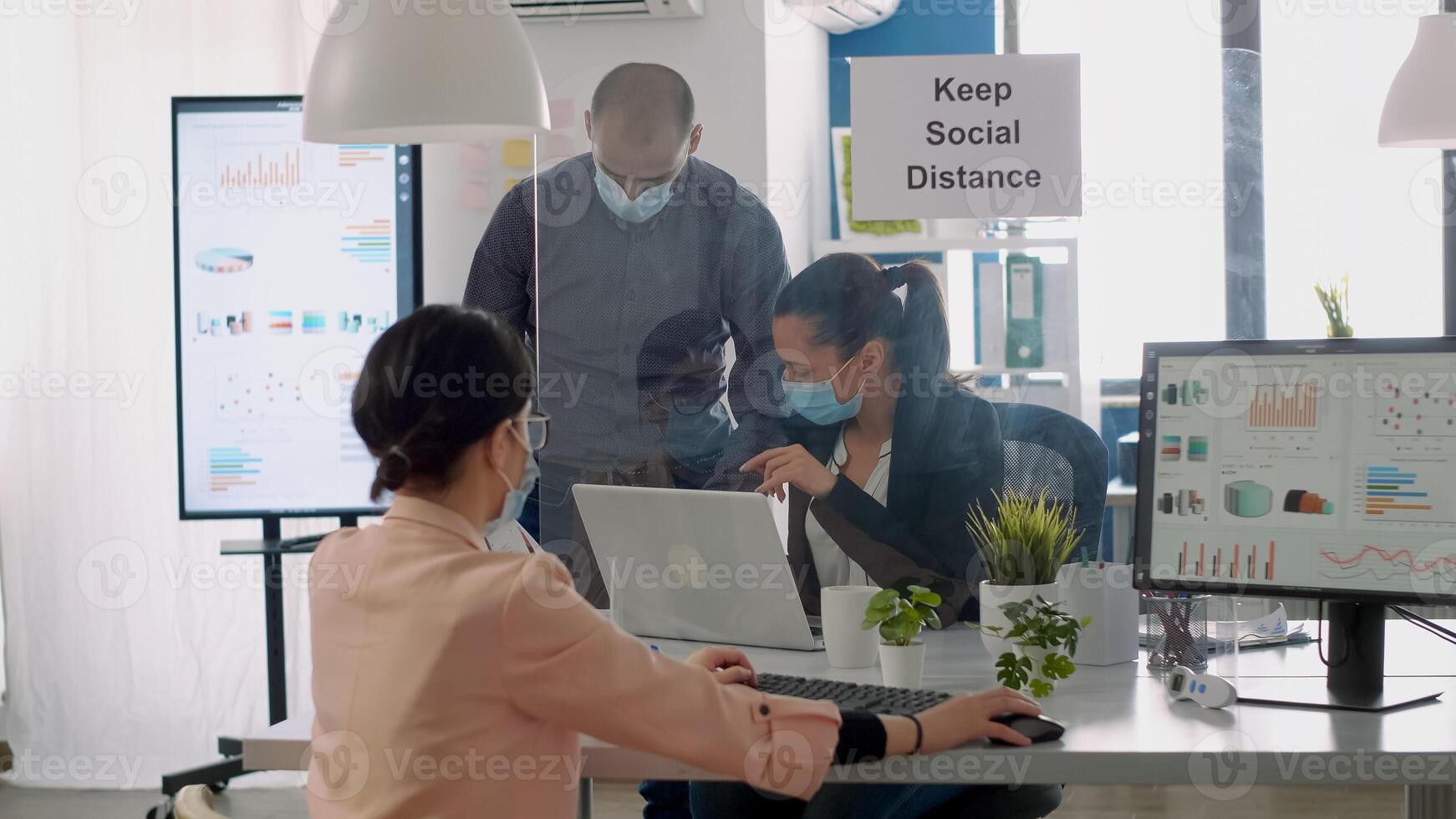 Team workers with protection face masks working in business office on computer during coronavirus lockdown. Coworkers keeping ing ing social distancing to avoid infection with virus disease photo