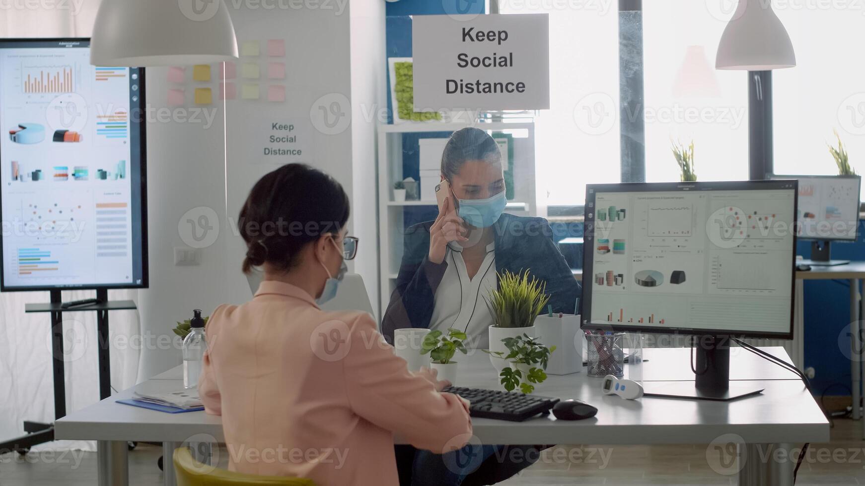 Freelancers with protection face masks working in new normal business office. Team discussing about financial company respecting social distance during coronavirus global pandemic photo